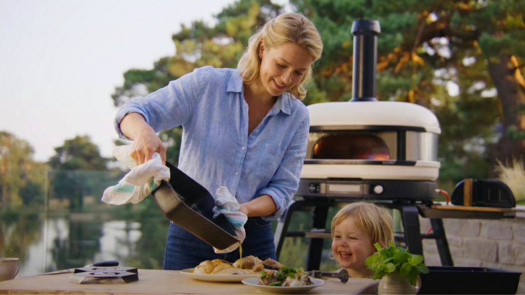 Frau bereitet Essen im Freien mit einem Gozney Pizzaofen zu, Kind schaut begeistert zu
