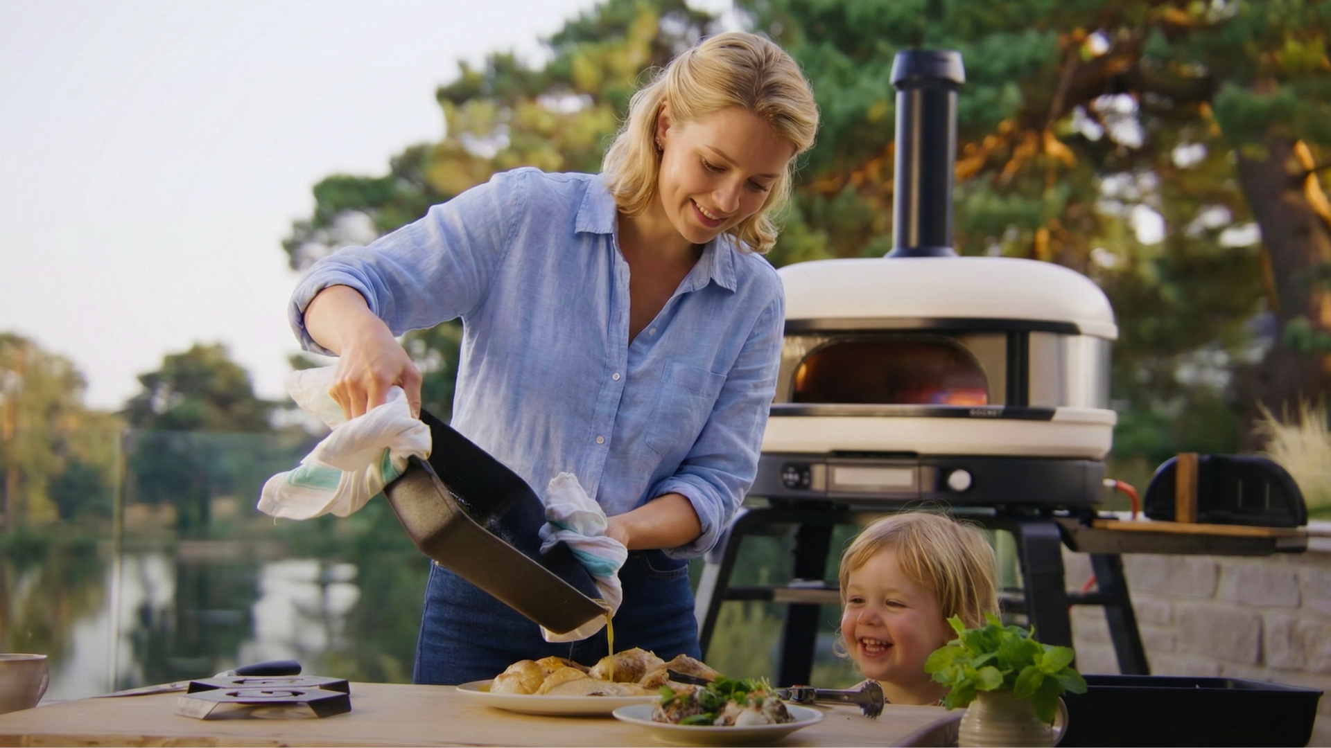 Frau bereitet Essen im Freien mit einem Gozney Pizzaofen zu, Kind schaut begeistert zu