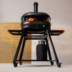 Gozney Dome Pizzaofen mit Rauchrohr auf Dome & Dome XL Gestell mit Holzablagen und Gasflasche unter dem Gestell in moderner Umgebung