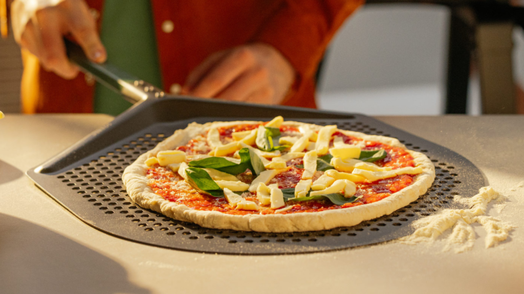 Eine belegte Pizza liegt auf einem Gozney Pro Pizzaschieber bereit zum Einschieben in den Pizzaofen